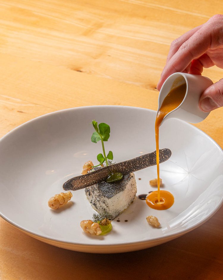 Außergewöhnliche Veranstaltungen im Jagdhof Hand gießt Sauce auf ein kunstvoll angerichtetes Gericht im weißen Teller