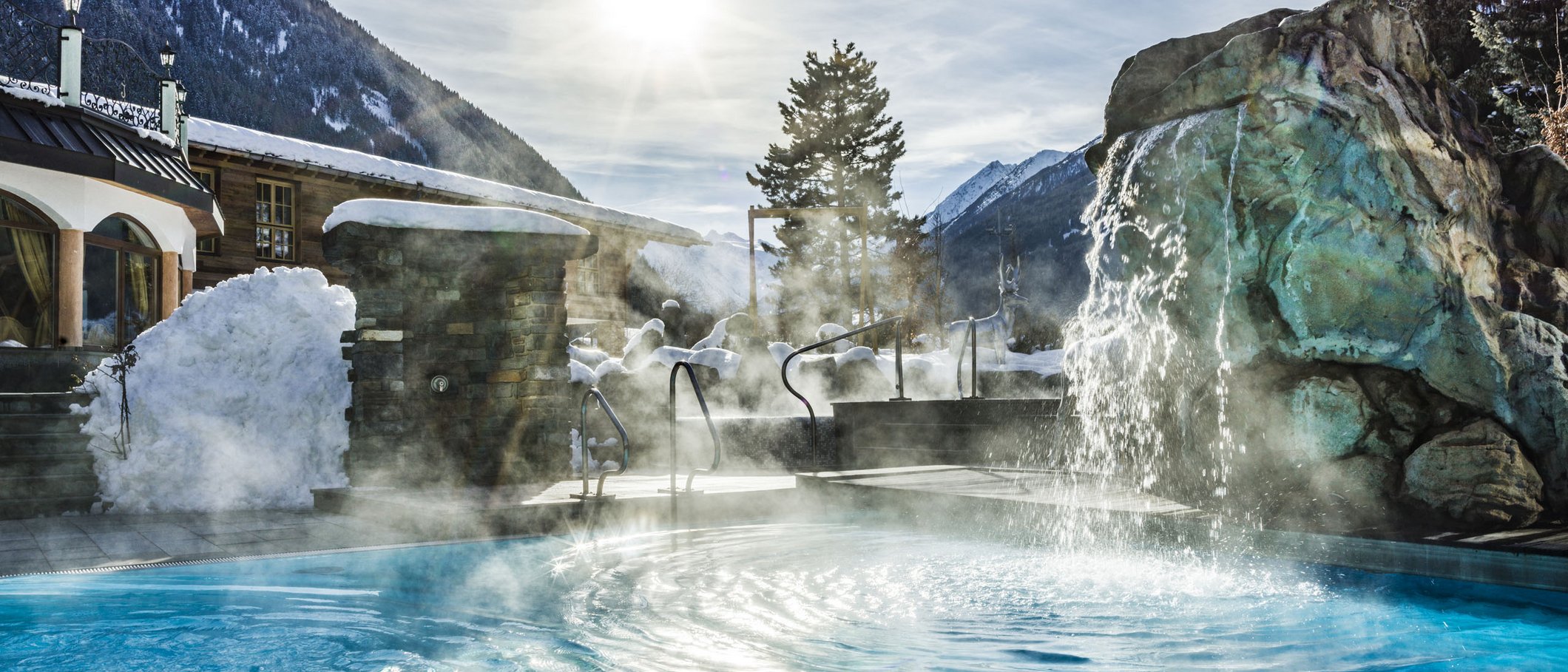Wie es sich für ein 5-Sterne-Hotel gehört: die Angebote. Outdoor Whirlpool mit Wasserfall in einer verschneiten Berglandschaft bei Sonnenschein