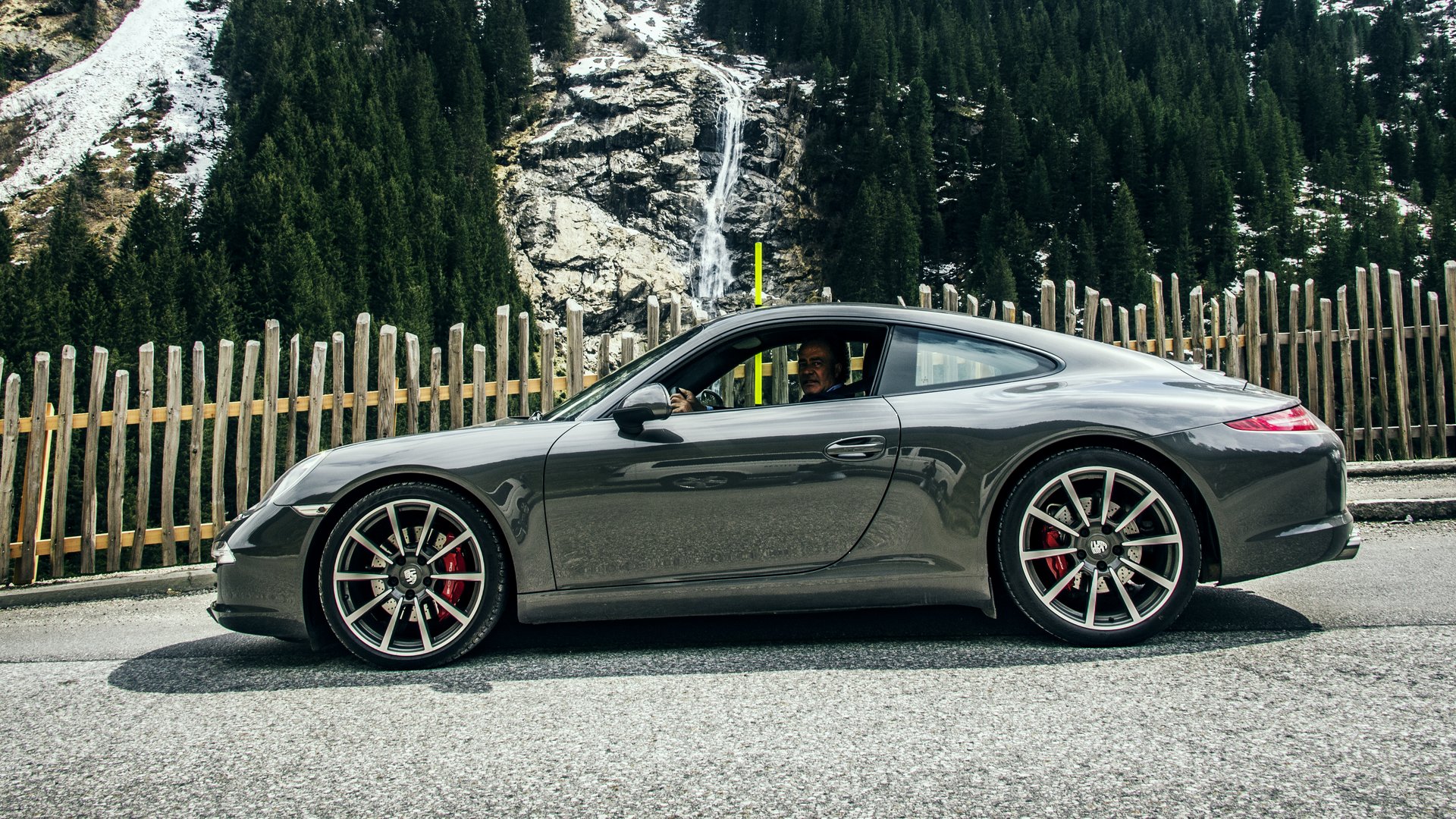 A highlight of the Jagdhof calendar: the Porsche Meetup Gray Porsche on mountain road with snowy pine trees and wooden fence