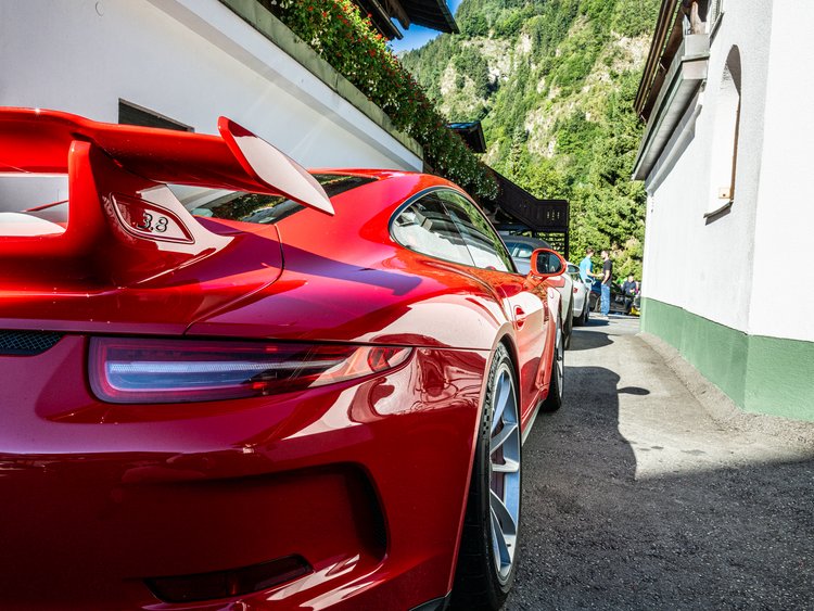 Außergewöhnliche Veranstaltungen im Jagdhof Roter Sportwagen hinten geparkt vor weißem Haus mit Bergen im Hintergrund