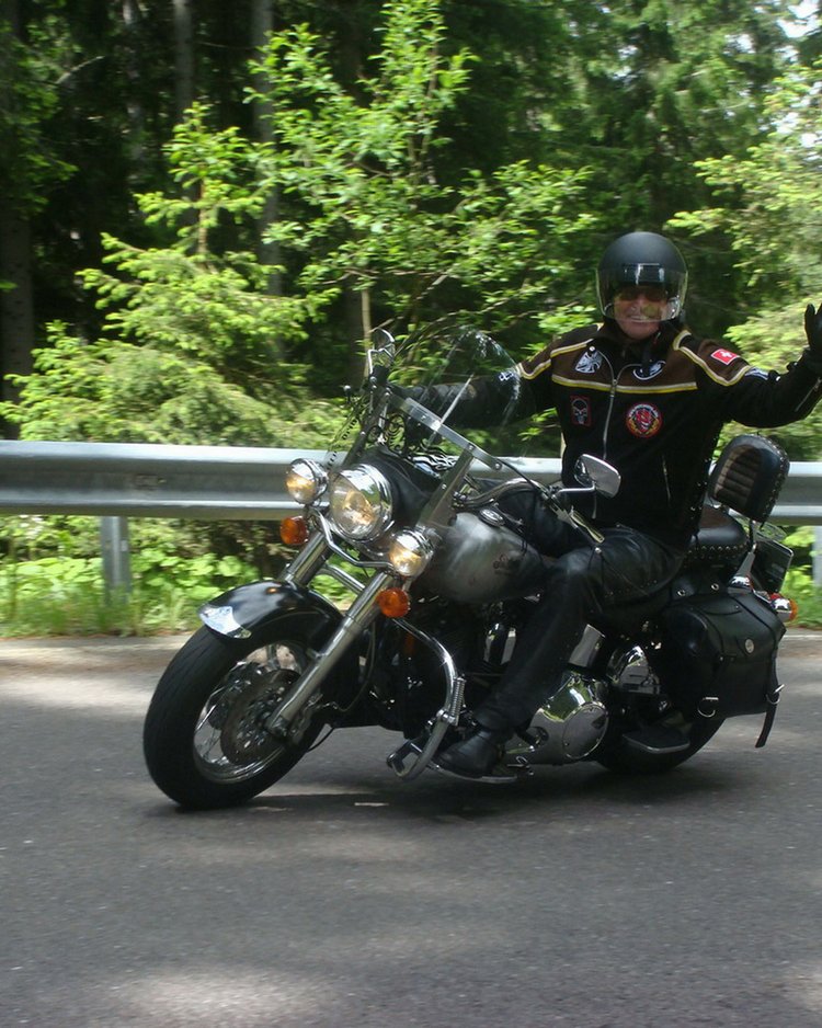 Außergewöhnliche Veranstaltungen im Jagdhof Motorradfahrer winkt auf kurviger Straße vor Wald