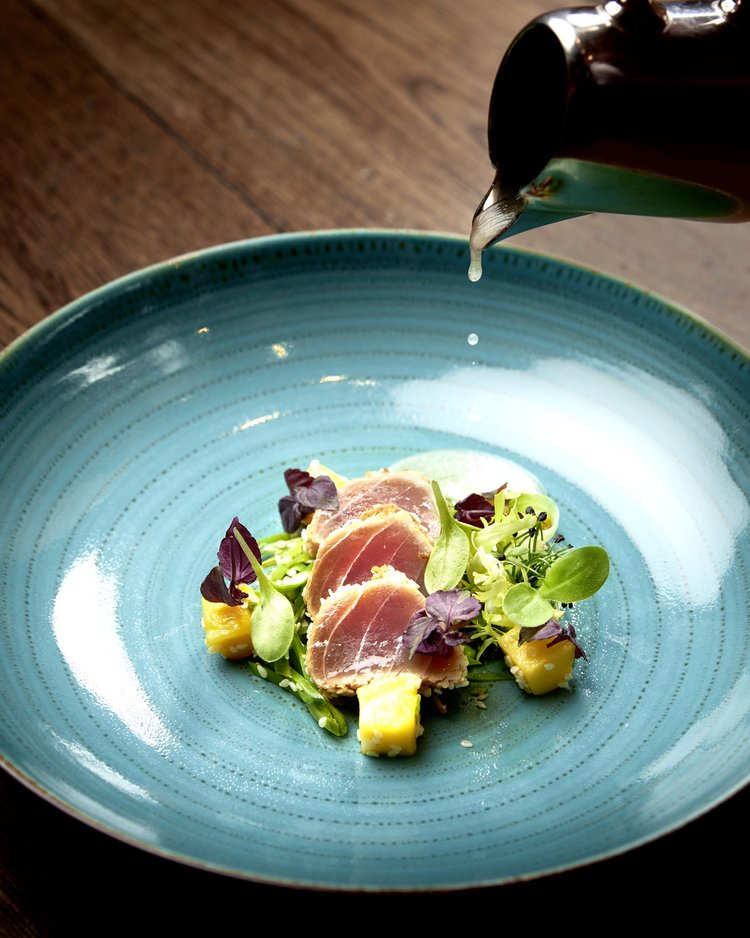 Außergewöhnliche Veranstaltungen im Jagdhof Fein angerichtete Vorspeise mit rohem Fisch, Mango und Blattsalat auf blauem Teller