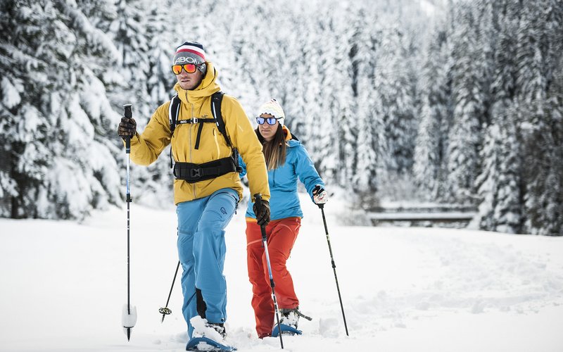 Wie es sich für ein 5-Sterne-Hotel gehört: die Angebote. Zwei Menschen beim Schneeschuhwandern in winterlicher Waldlandschaft