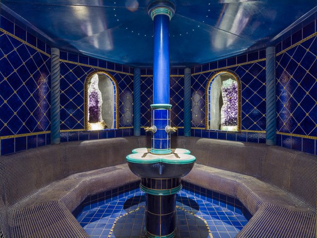 Auf in Ihr De-luxe-Wellnesshotel im Stubaital Blau gekachelter Dampfbadraum mit gebogenem Sitzbereich und zentraler Säule
