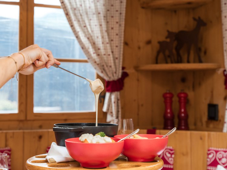 The Fondue Gondola: a unique experience at the Jagdhof Hand holding cheese fondue fork with cheese above black pot
