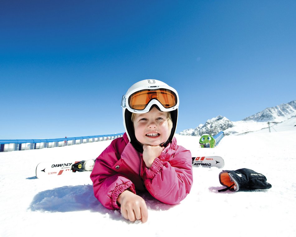 Willkommen im einzigen 5-Sterne-Hotel im Stubaital! Kind in Skihelm und pinker Jacke liegt im Schnee mit Ski und Handschuhen