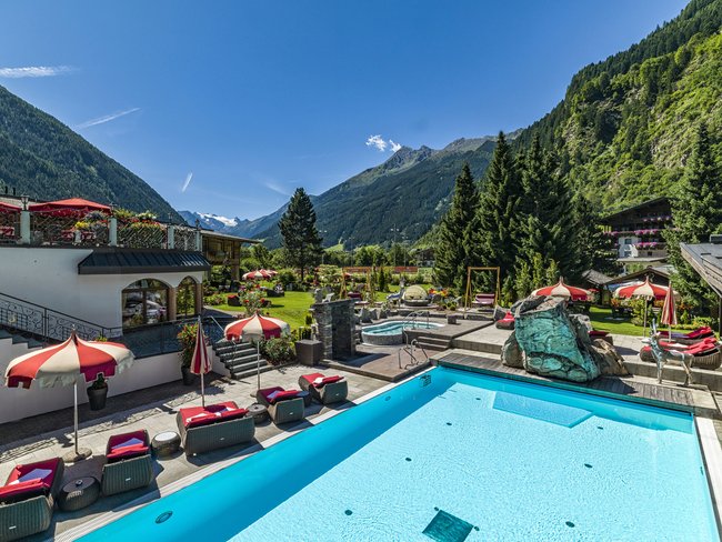 Auf in Ihr De-luxe-Wellnesshotel im Stubaital Pool mit Sonnenliegen und Berglandschaft im Hintergrund
