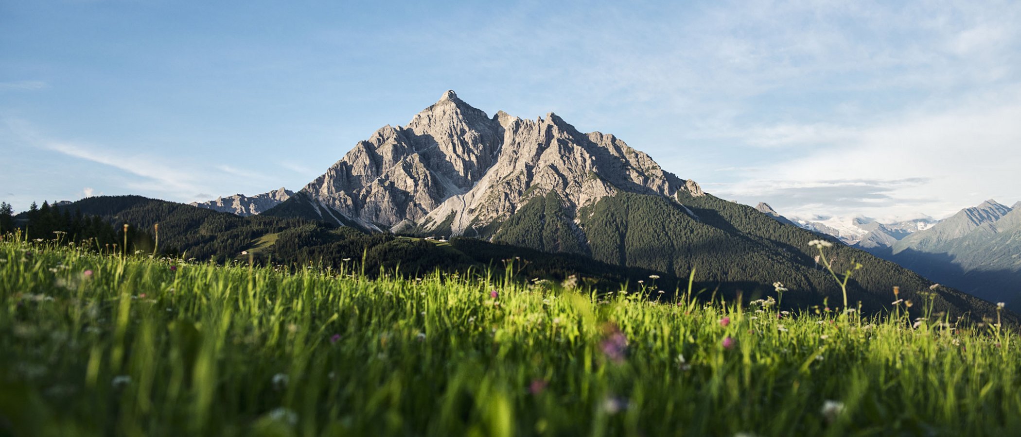 Willkommen im einzigen 5-Sterne-Hotel im Stubaital! Berggipfel mit grüner Wiese im Vordergrund unter blauem Himmel