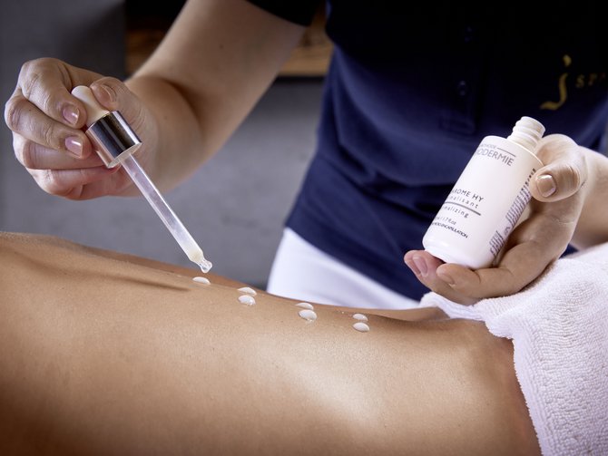 Your wellness treatments at the Jagdhof Therapist applying lotion with dropper onto a bare back