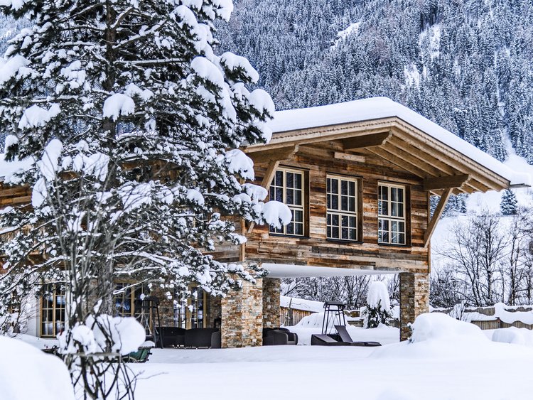 Auf in Ihr De-luxe-Wellnesshotel im Stubaital Holzhaus im Schnee vor bewaldetem Berg im Winter