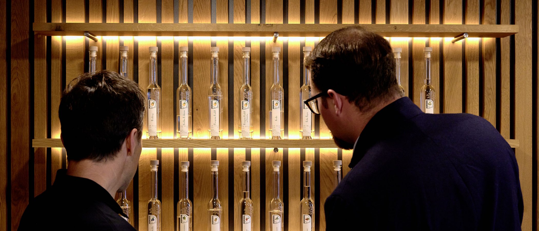The Fondue Gondola: a unique experience at the Jagdhof Two men look at a lit wooden shelf wall with clear bottles