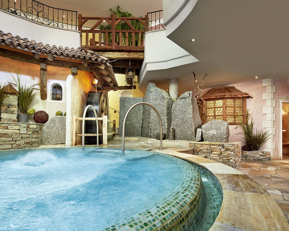 Willkommen im einzigen 5-Sterne-Hotel im Stubaital! Innenraum eines luxuriösen Spapools mit Steindekor und Wasserrad