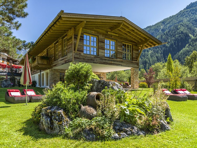 Auf in Ihr De-luxe-Wellnesshotel im Stubaital Holzhaus auf Stelzen mit Garten und Liegestühlen vor Bergkulisse