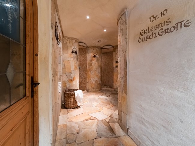 Auf in Ihr De-luxe-Wellnesshotel im Stubaital Eingang zu Erlebnis-Dusch-Grotte mit Steinfliesen und Korb mit Handtuch