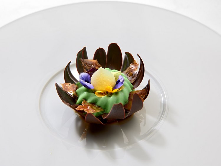 Eines der besten Haubenrestaurants in Tirol Elegantes Dessert mit grüner Creme, Schokolade und essbaren Blüten auf weißem Teller