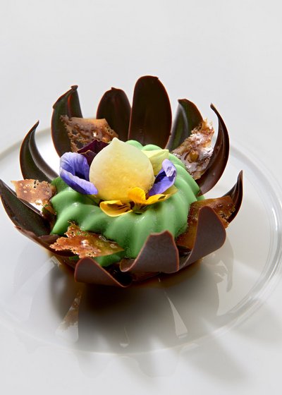 Willkommen im einzigen 5-Sterne-Hotel im Stubaital! Elegantes Dessert mit grüner Creme, Schokolade und essbaren Blüten auf weißem Teller