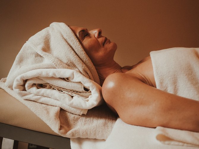 Your wellness treatments at the Jagdhof Woman relaxing on massage table with towels supporting her head